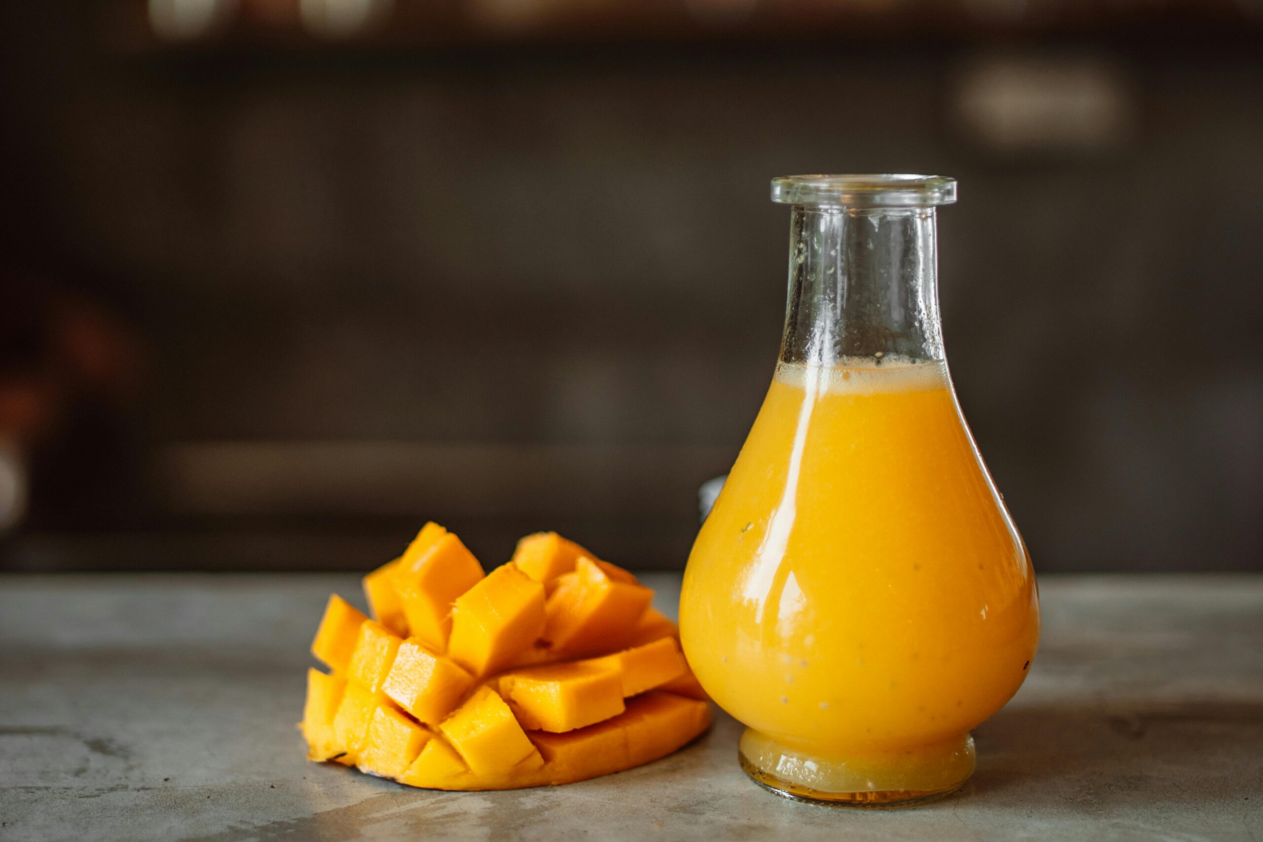 pexels photo 4955257 4955257 A refreshing and vibrant mango juice served in a clear glass bottle next to ripe mangos.