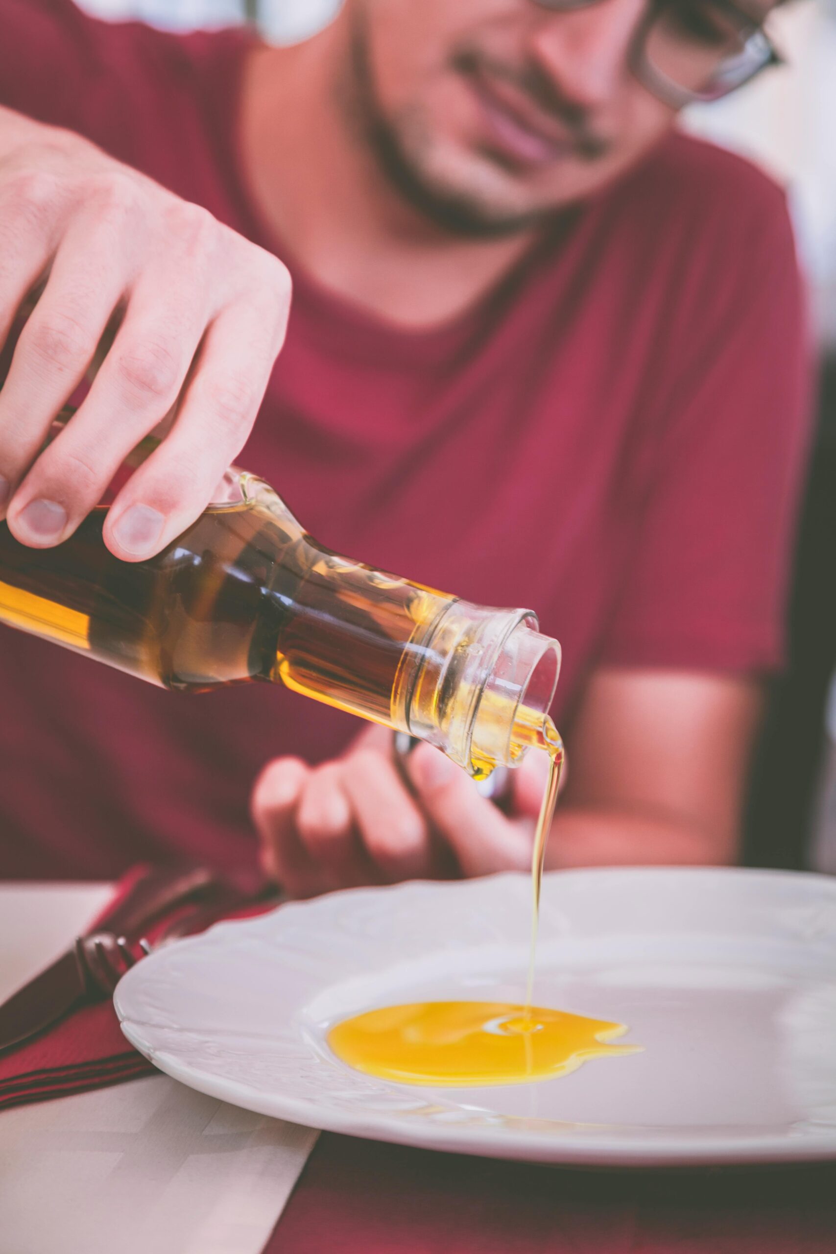 Home Man pouring olive oil onto a plate indoors, perfect for culinary and healthy eating themes.